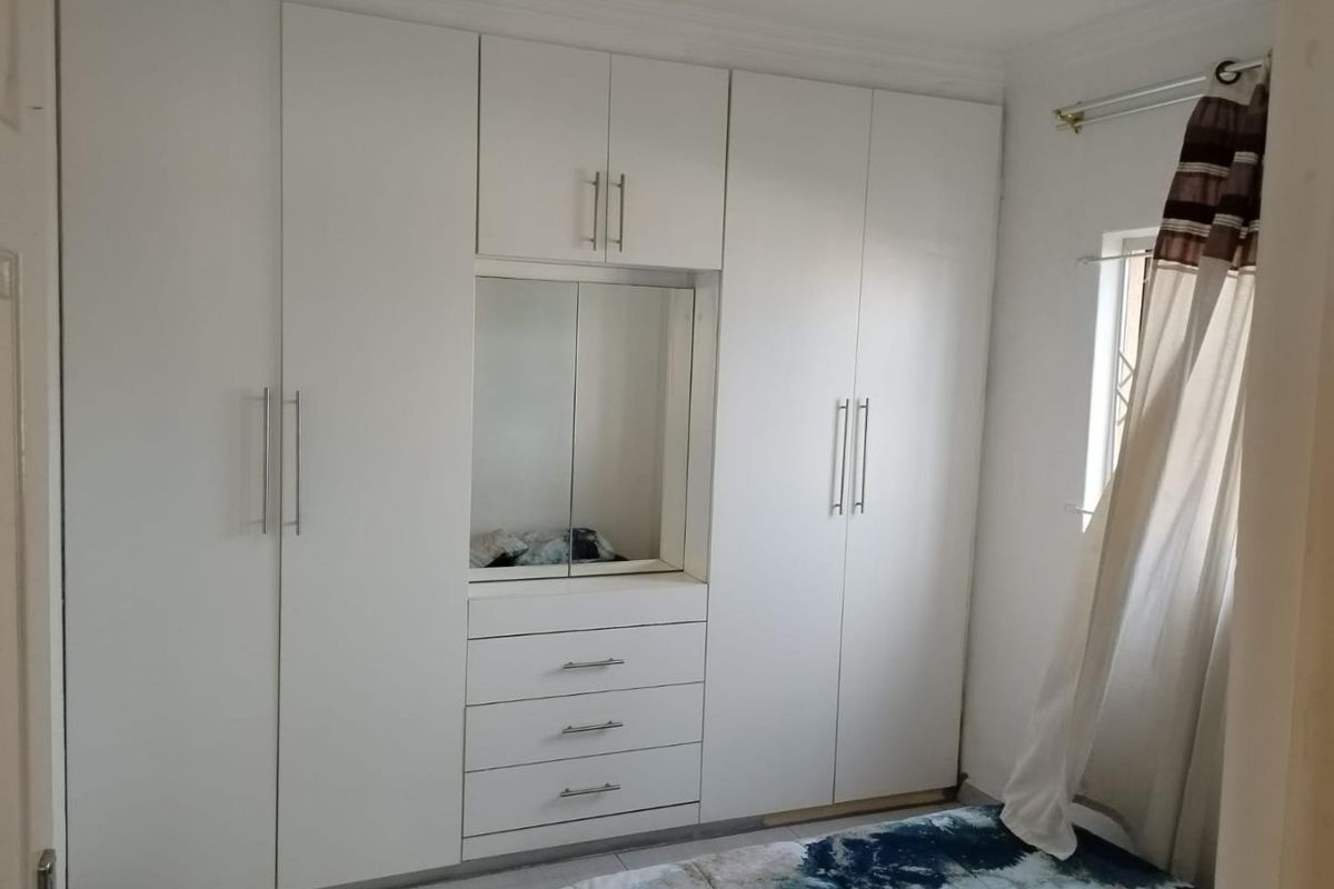 A bedroom featuring white built-in cupboards with integrated vanity mirror and drawers, providing ample storage space.
