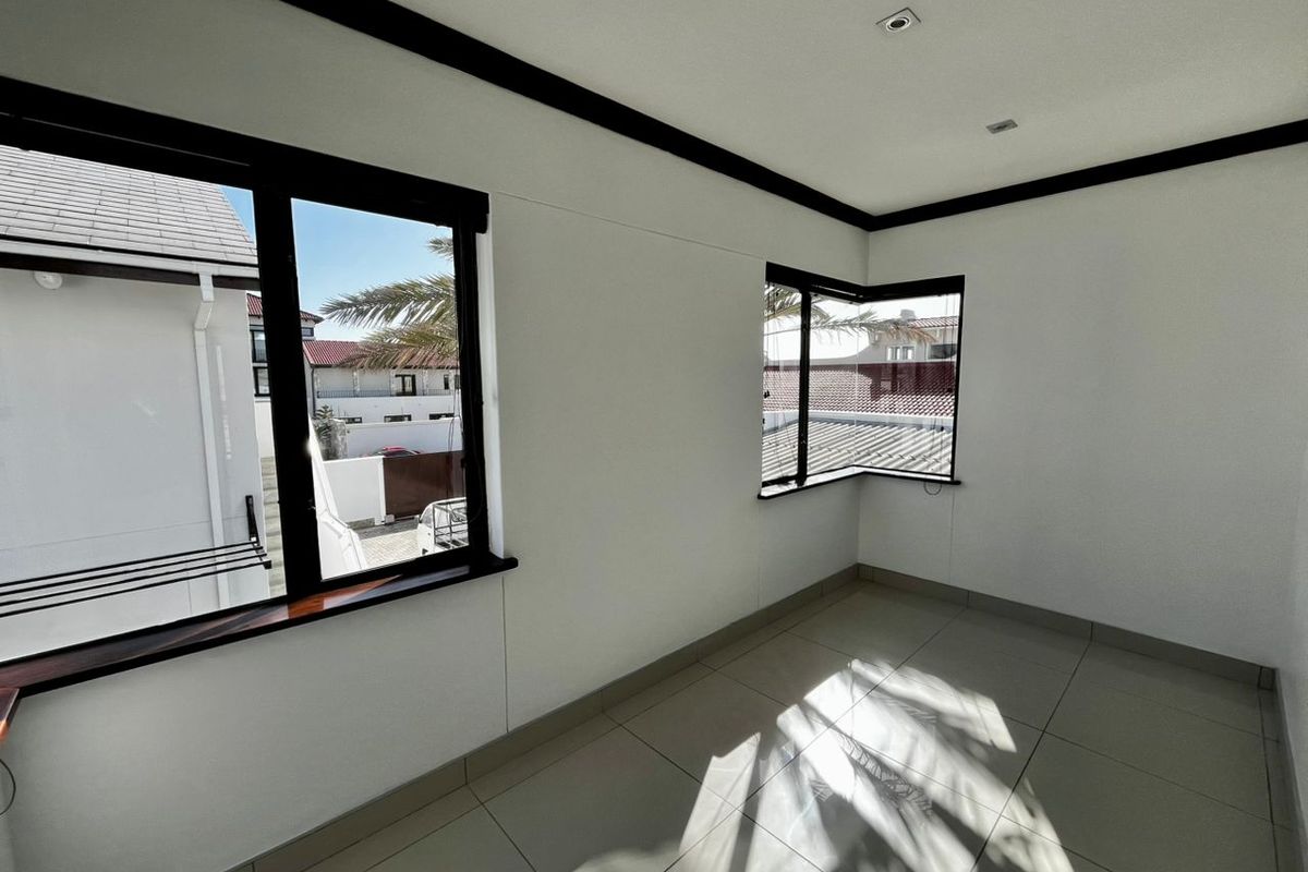 A bright, empty bedroom featuring tiled flooring, modern black-framed windows, and recessed ceiling lighting, offering a clean and neutral space.