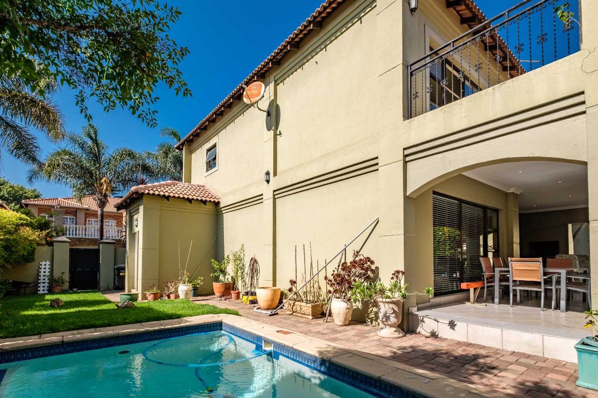 Rear view of the property featuring a swimming pool, paved patio area, and a balcony overlooking the garden.