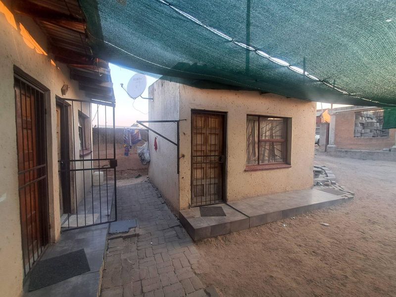 Rear exterior view showing a paved walkway, security gates, and a shade cloth canopy covering the outdoor area.