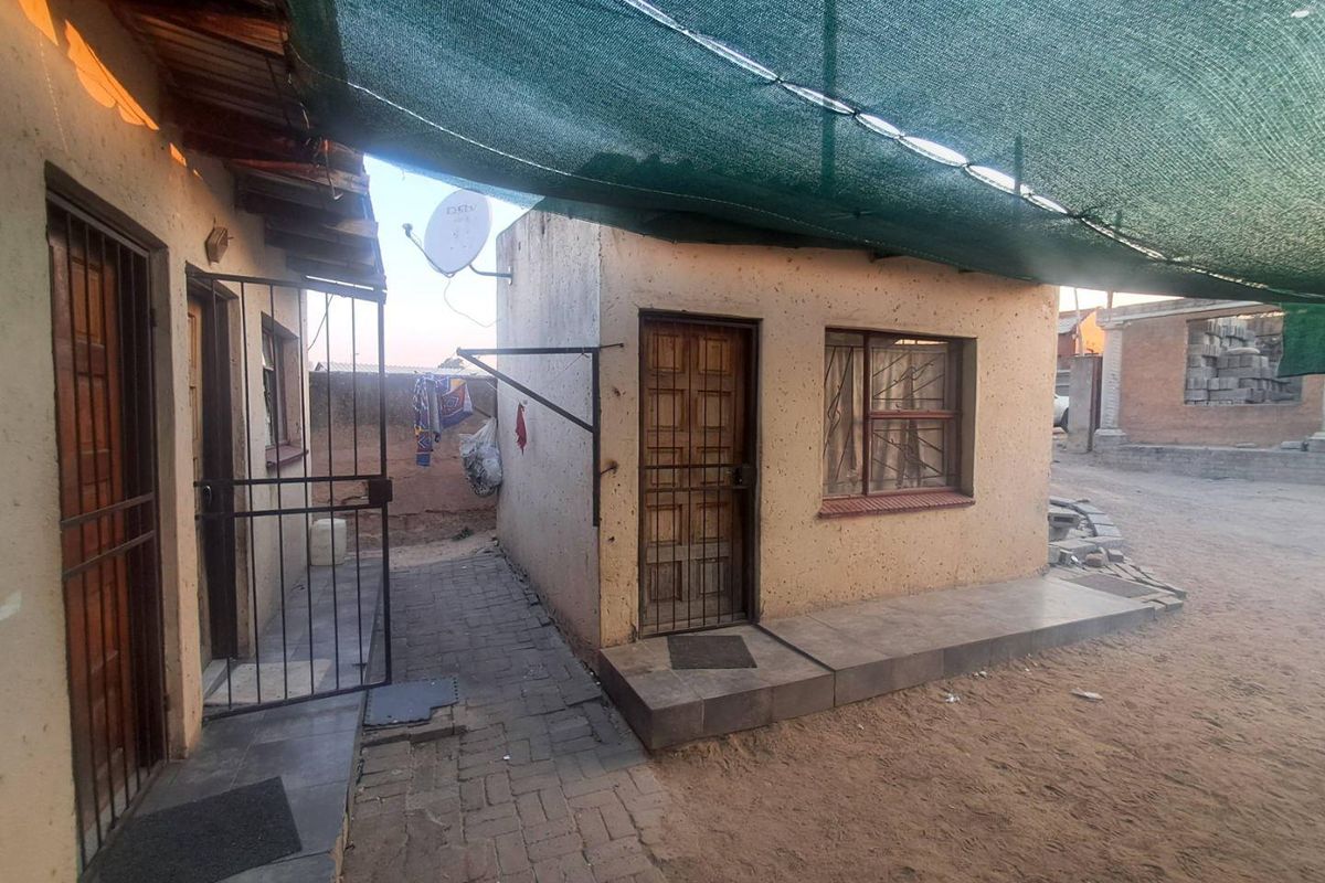 Rear exterior view showing a paved walkway, security gates, and a shade cloth canopy covering the outdoor area.