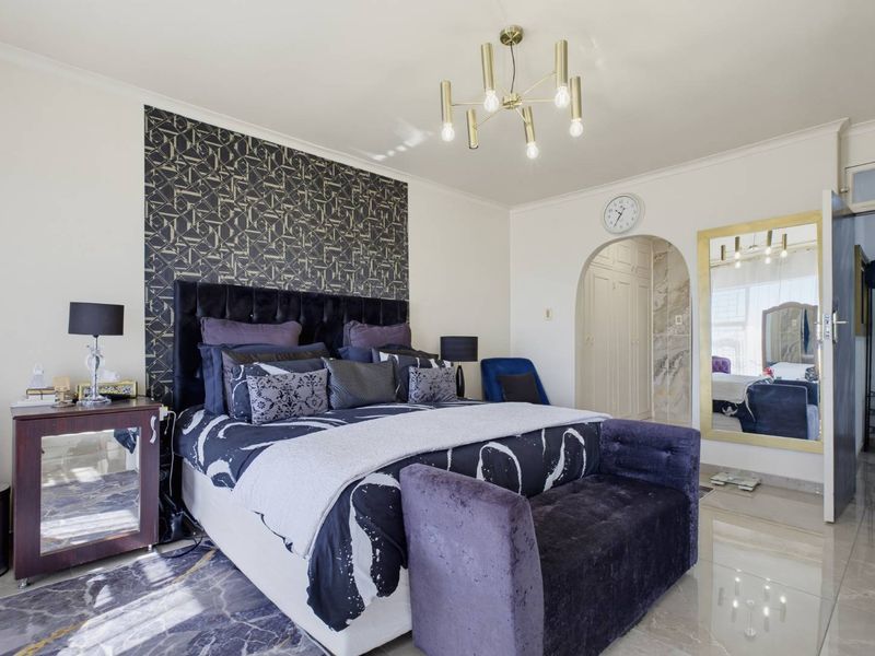 A well-maintained bedroom featuring a modern chandelier, arched doorway leading to built-in storage, and polished tiled flooring.