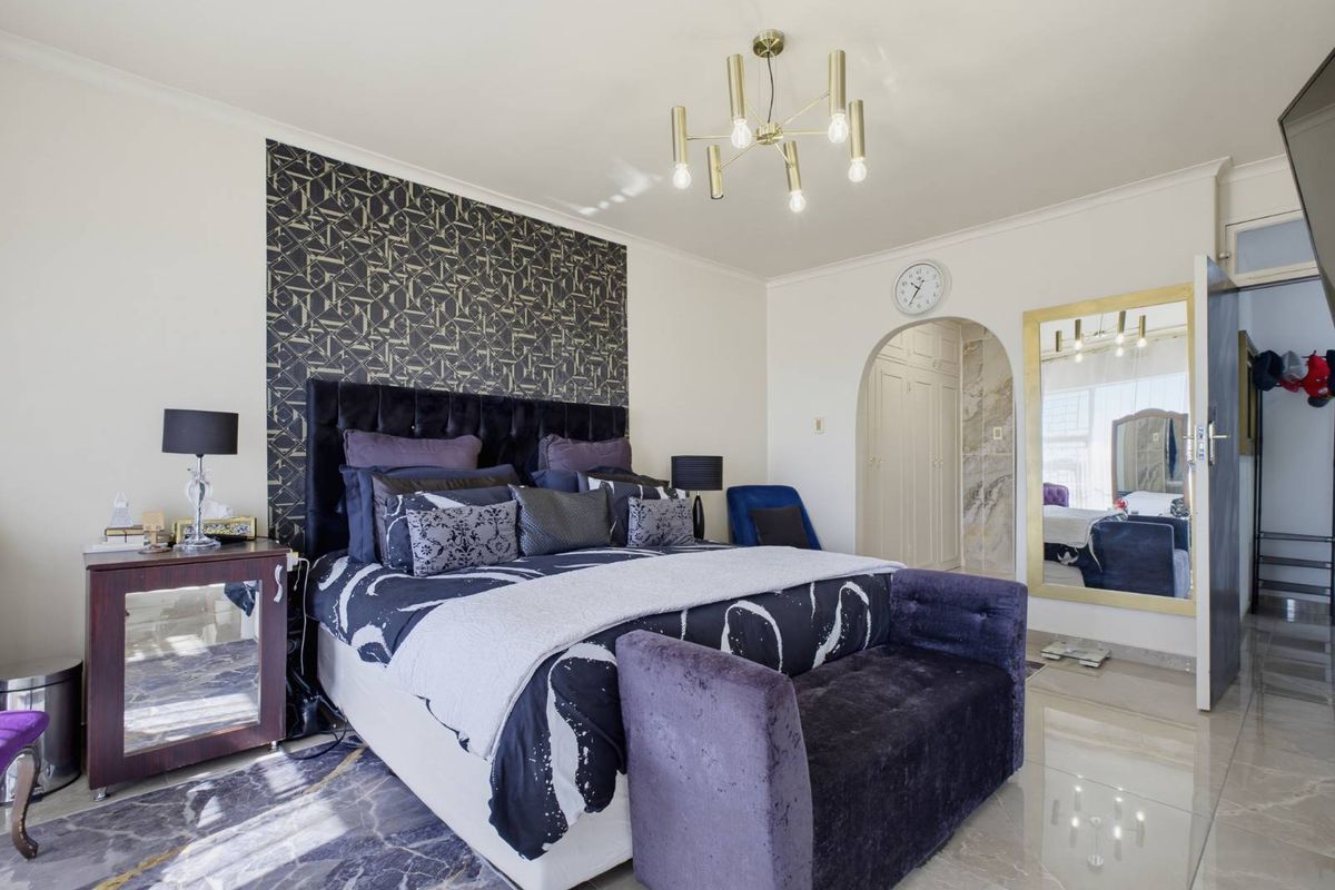 A well-maintained bedroom featuring a modern chandelier, arched doorway leading to built-in storage, and polished tiled flooring.