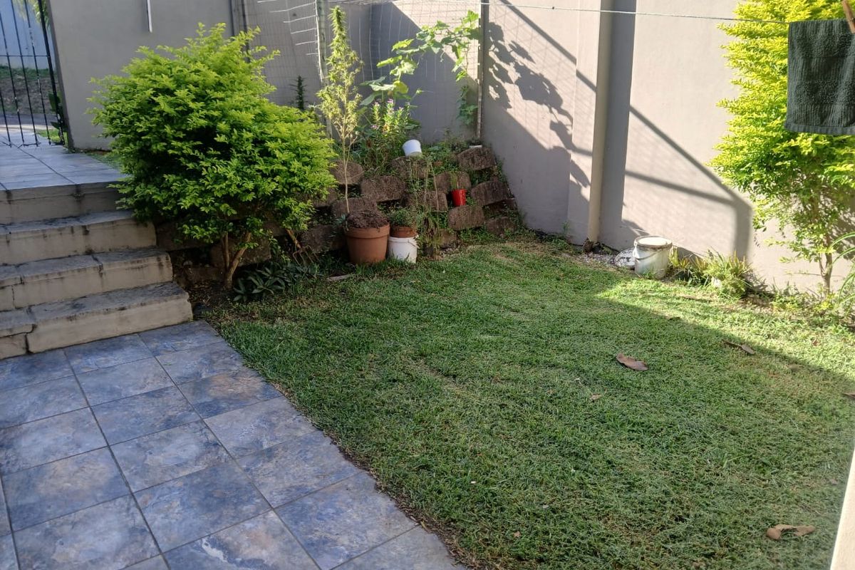 A compact rear garden area featuring a tiled patio, concrete steps, and a small lawn enclosed by a boundary wall.