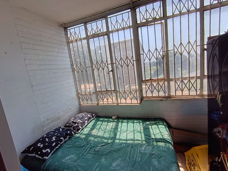 A bedroom featuring painted brick walls and large windows with integrated metal security gates, offering natural light and an urban view.