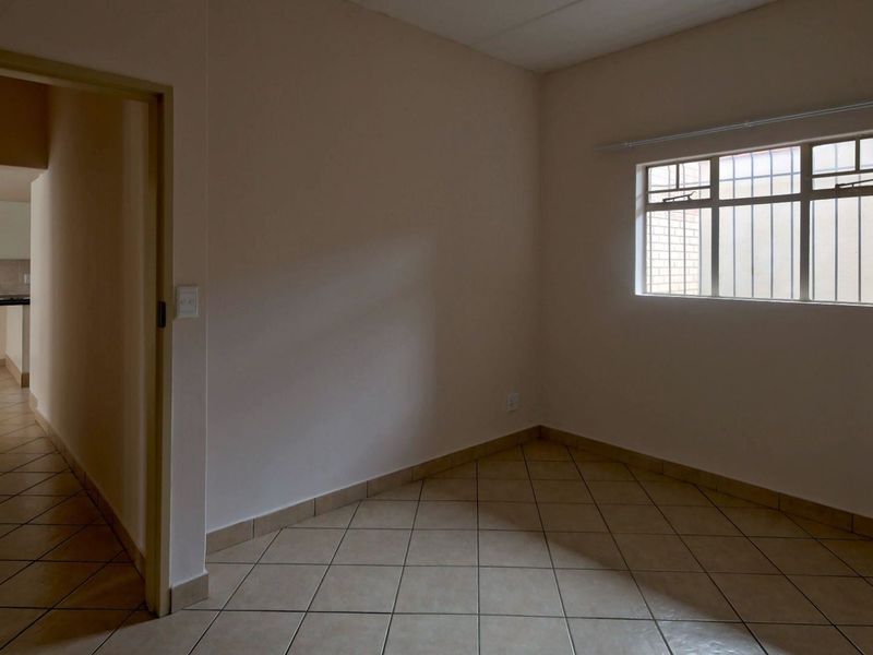 An empty bedroom featuring tiled flooring and a window with security bars, offering a neutral space ready for personalization.