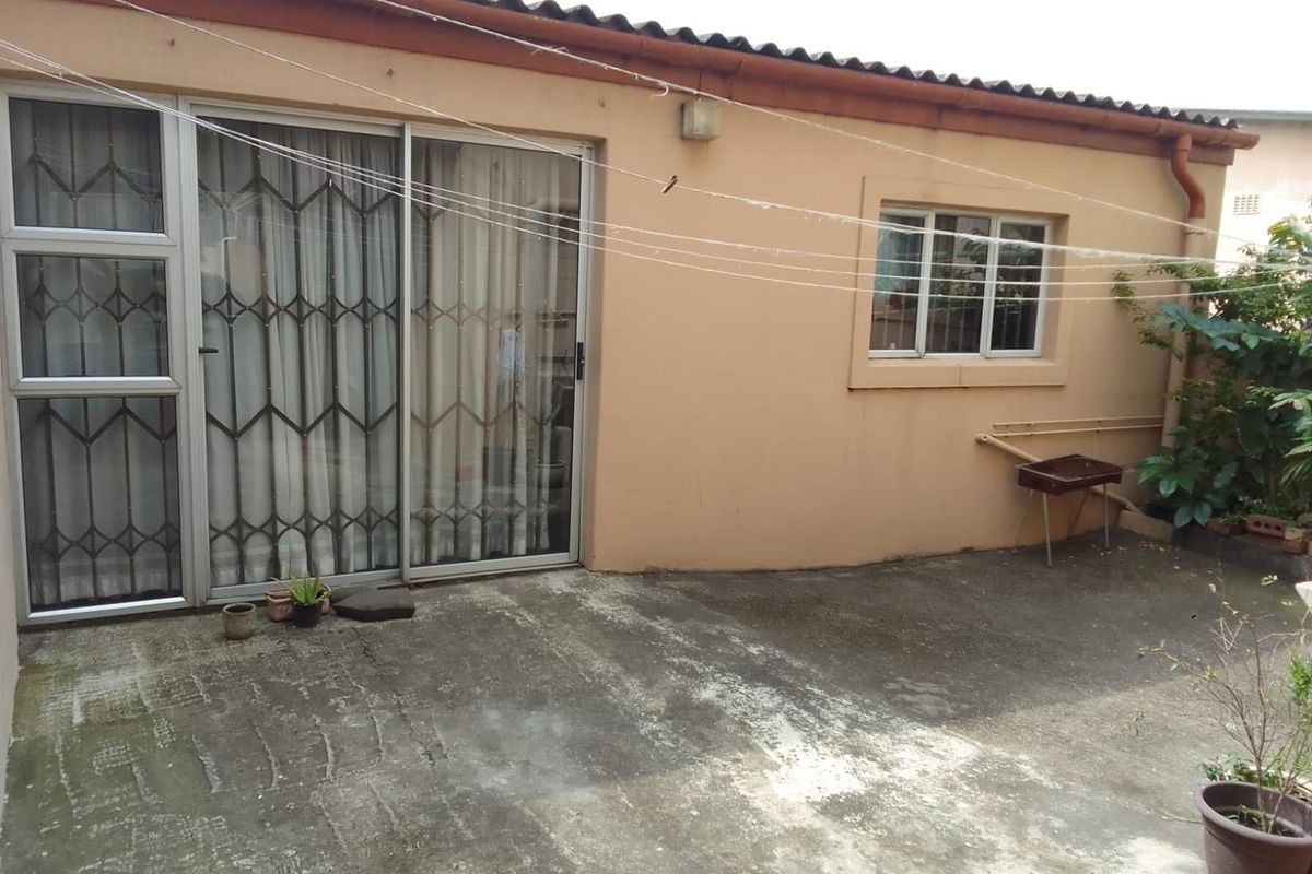 Rear exterior view of the property featuring a concrete patio area, sliding glass doors with security gates, and a tiled roof.
