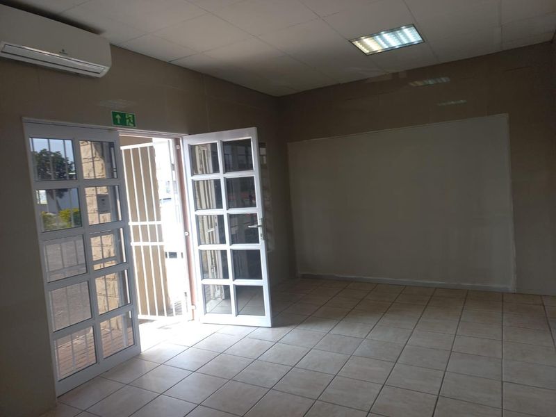 An empty office space featuring tiled flooring, recessed lighting, a split-system air conditioner, and glass panelled double doors with an external security gate.