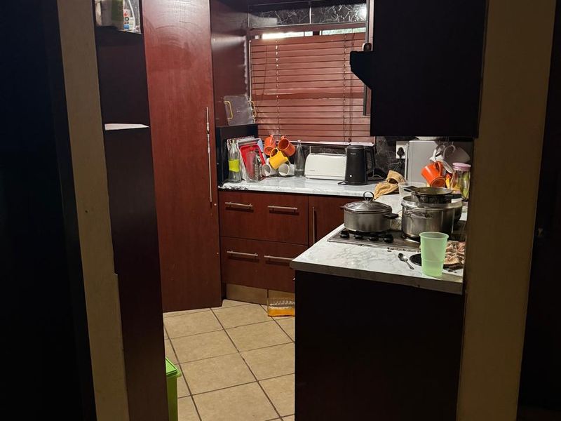 A compact kitchen featuring dark wood cabinetry, laminate countertops, a gas hob, and distinctive decorative ceiling tiles with tiled flooring throughout.