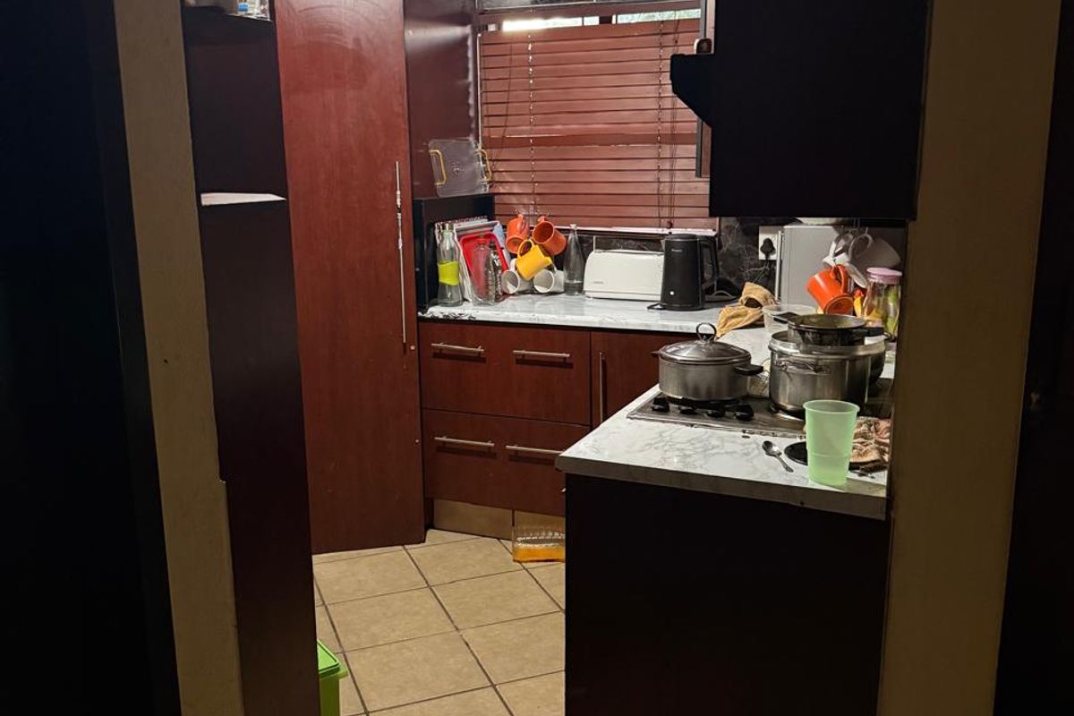A compact kitchen featuring dark wood cabinetry, laminate countertops, a gas hob, and distinctive decorative ceiling tiles with tiled flooring throughout.