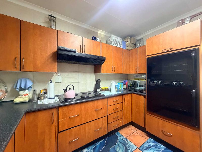 A functional kitchen featuring wood-look laminate cabinetry, built-in oven, electric hob, extractor fan, and tiled backsplash with durable countertops.