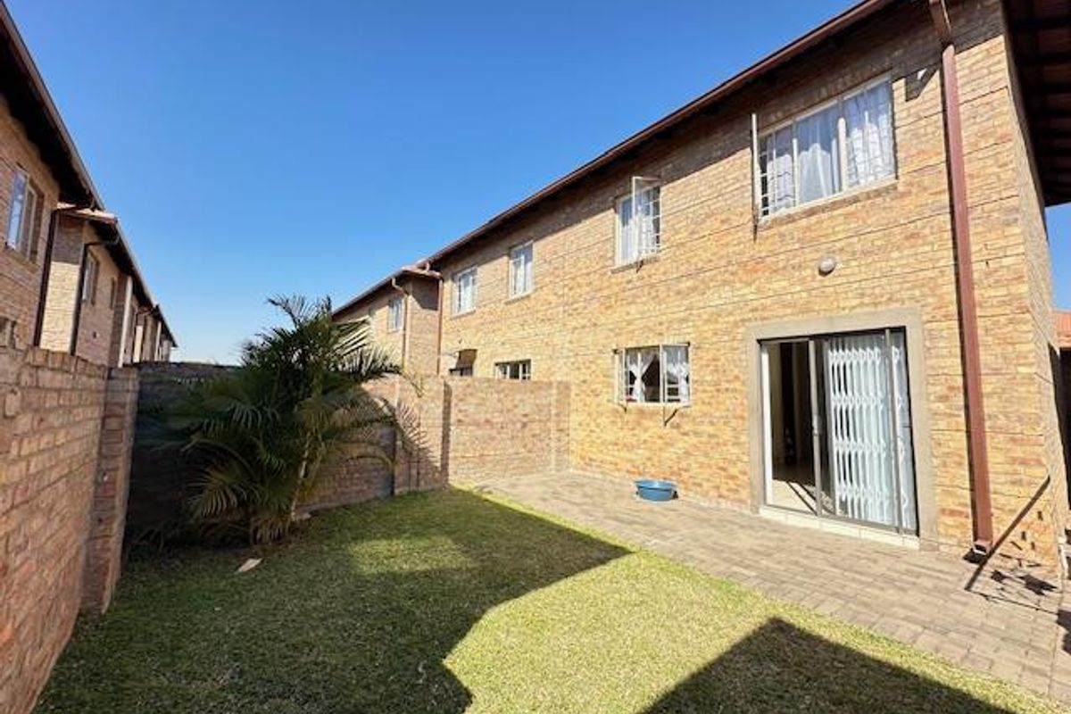 Rear view of the townhouse featuring a private garden, paved patio area, and sliding glass doors with security gates.