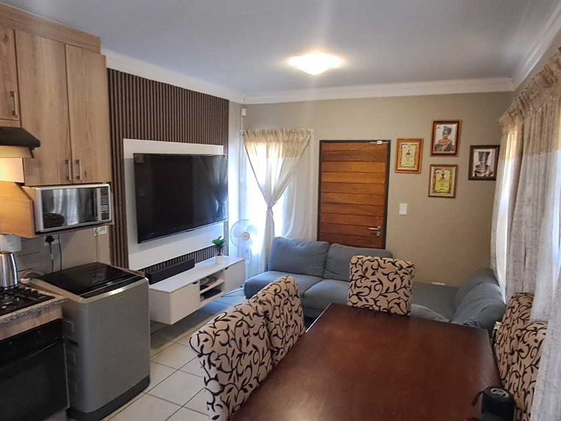 Open-plan living area featuring a modern kitchen with built-in appliances, tiled flooring, and a feature wall with integrated television mounting.
