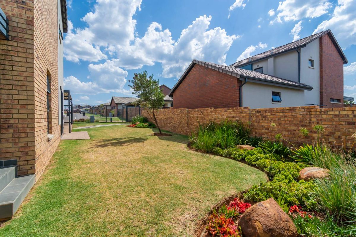 A well-maintained rear garden featuring a manicured lawn, landscaped flower beds with rock accents, and a brick boundary wall in a residential estate setting.