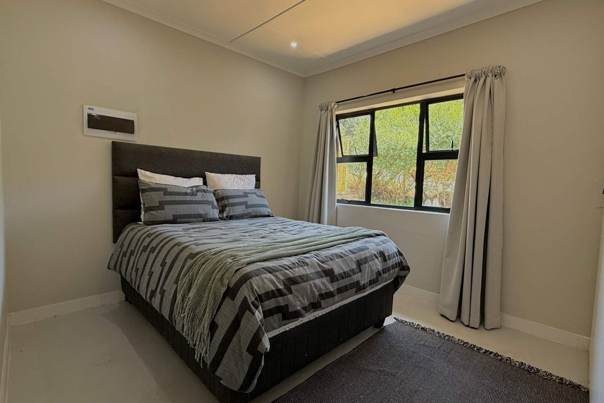 A well-maintained bedroom featuring neutral wall tones, a large aluminium-framed window, and recessed ceiling lighting.