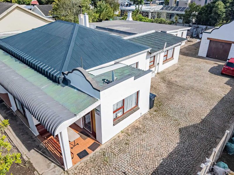 Aerial view of the property showing the main house with a corrugated metal roof, a covered patio area, and an extensive paved driveway leading to a garage.