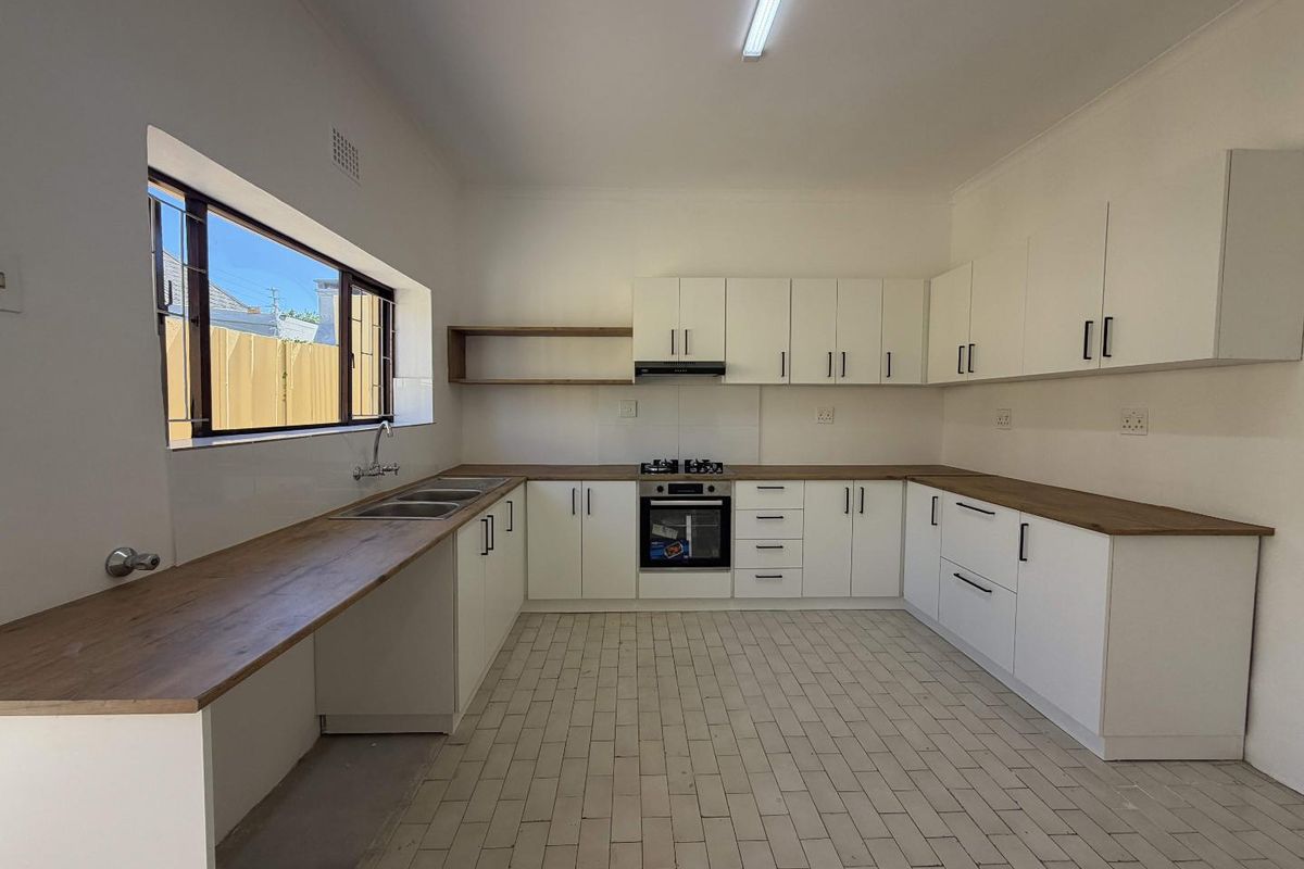 A clean, modern kitchen featuring white cabinetry, wooden countertops, a built-in oven, gas hob, and tiled flooring in a bright, open space.