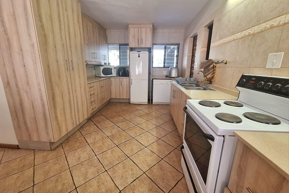 Functional kitchen featuring light wood-look cabinetry, tiled flooring, tiled splashbacks, and a freestanding electric stove.
