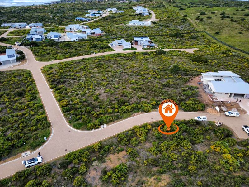 Aerial view of a vacant residential plot in a coastal estate, featuring established paved roads and surrounding natural vegetation.