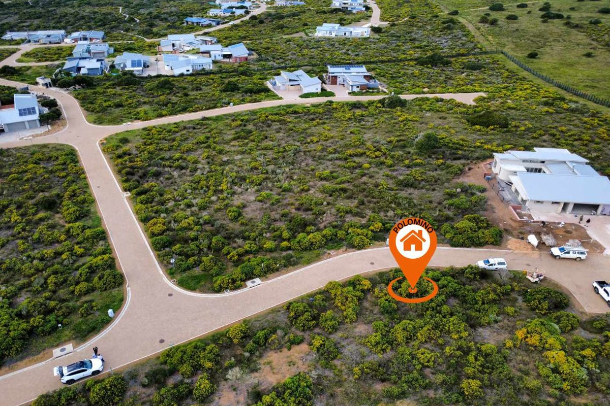 Aerial view of a vacant residential plot in a coastal estate, featuring established paved roads and surrounding natural vegetation.