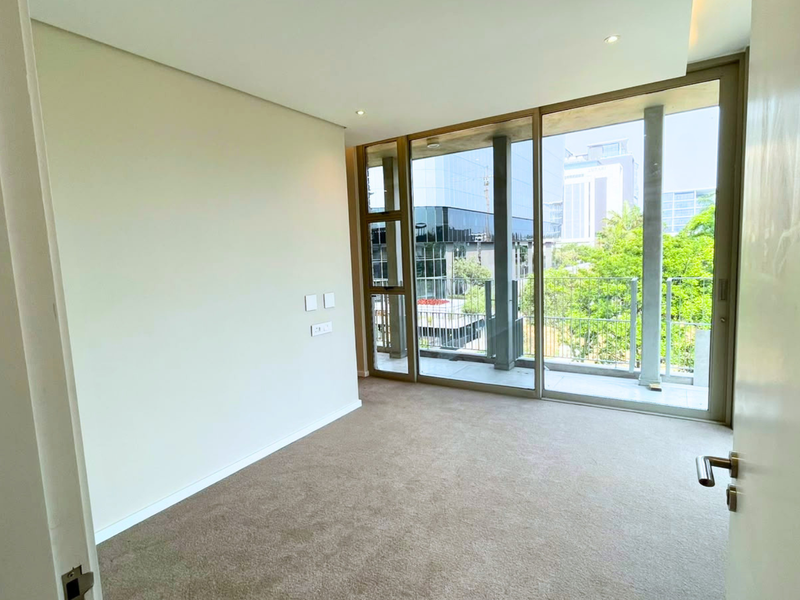A bright, empty bedroom featuring floor-to-ceiling windows, sliding glass doors leading to a balcony, and neutral carpeted flooring.