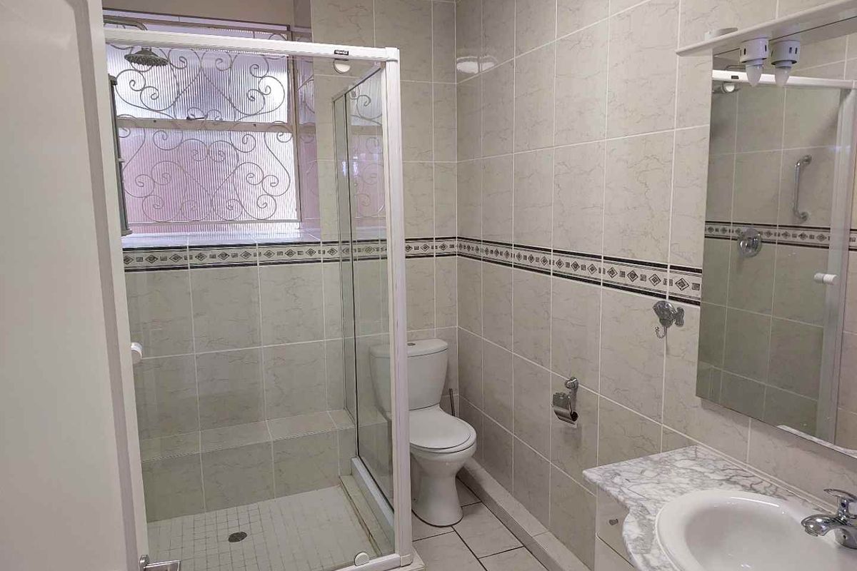 A functional bathroom featuring a shower enclosure, toilet, and a vanity with an integrated basin, finished with neutral wall and floor tiles.