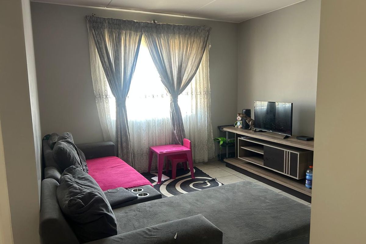 A functional living room featuring tiled flooring and a large window with curtain tracks, providing a comfortable and practical space for daily living.