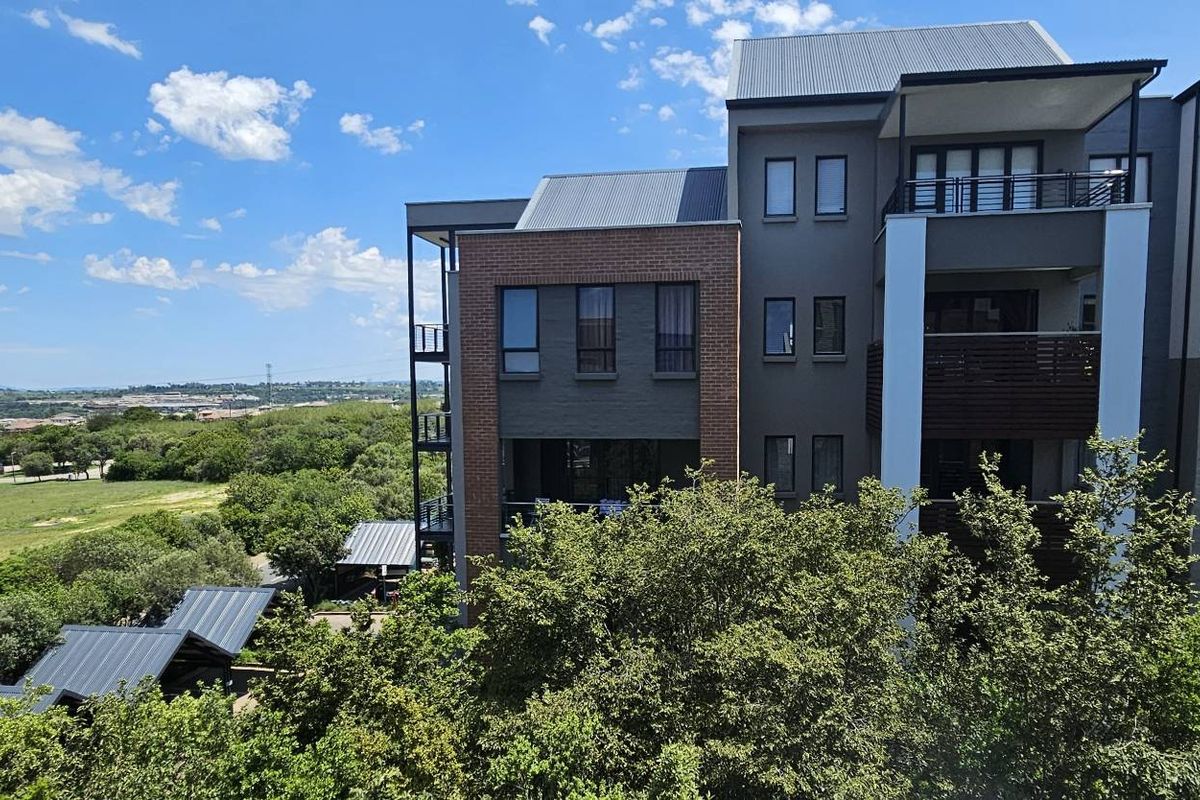 A view of the rear elevation of a modern apartment building featuring brick and painted finishes, metal roofing, and private balconies overlooking green space.