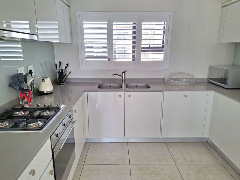 Modern kitchen featuring white gloss cabinetry, stone countertops, a gas hob, built-in oven, and plantation shutters over the window.