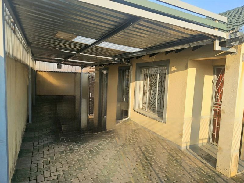 A covered outdoor patio area featuring paved flooring, a corrugated metal roof, and security bars on the windows.