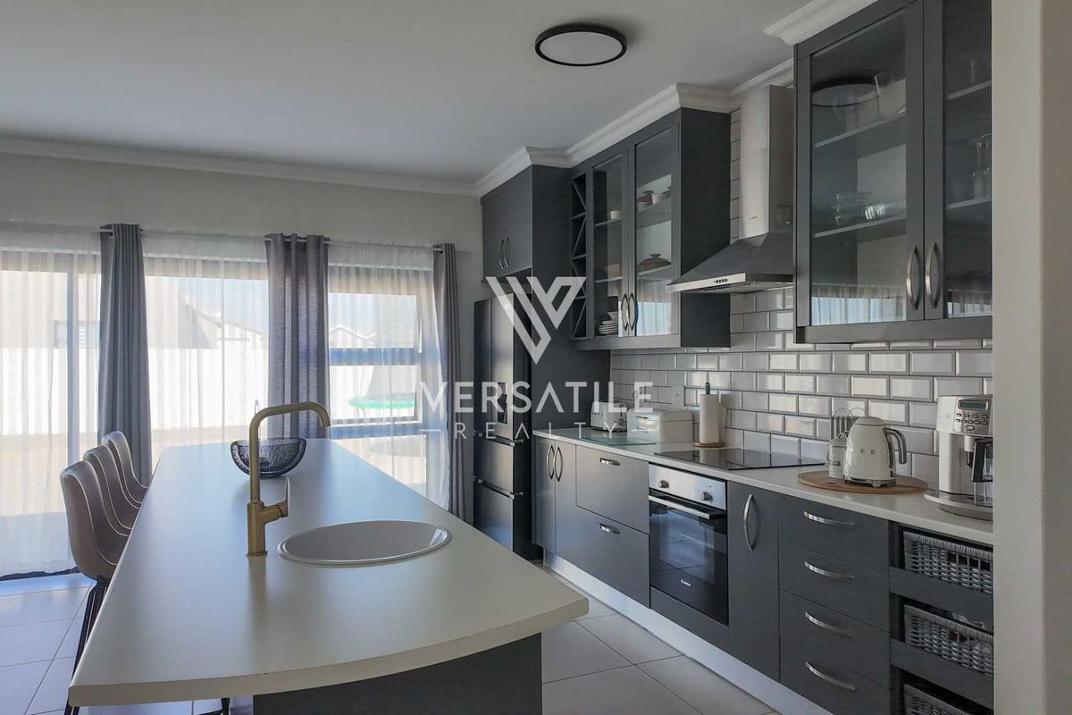 Modern kitchen featuring dark cabinetry, subway tile backsplash, a central island with a brass faucet, and integrated appliances.