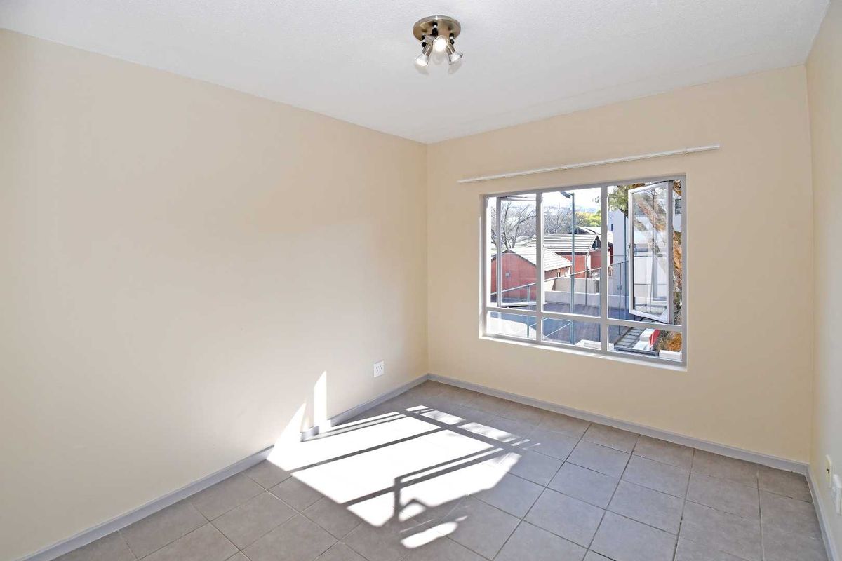 A bright, empty bedroom featuring neutral wall paint, tiled flooring, and a large window providing natural light and an exterior view.
