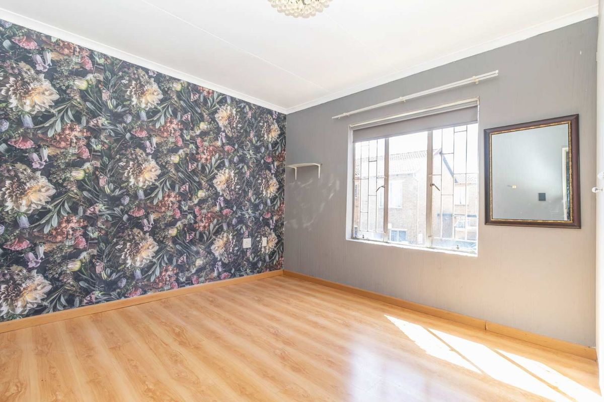 A bright bedroom featuring laminate flooring, a floral feature wall, and security bars on the window.
