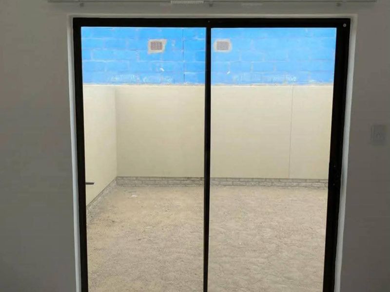 An empty interior space featuring tiled flooring and a sliding glass door leading to a private, walled outdoor courtyard area.