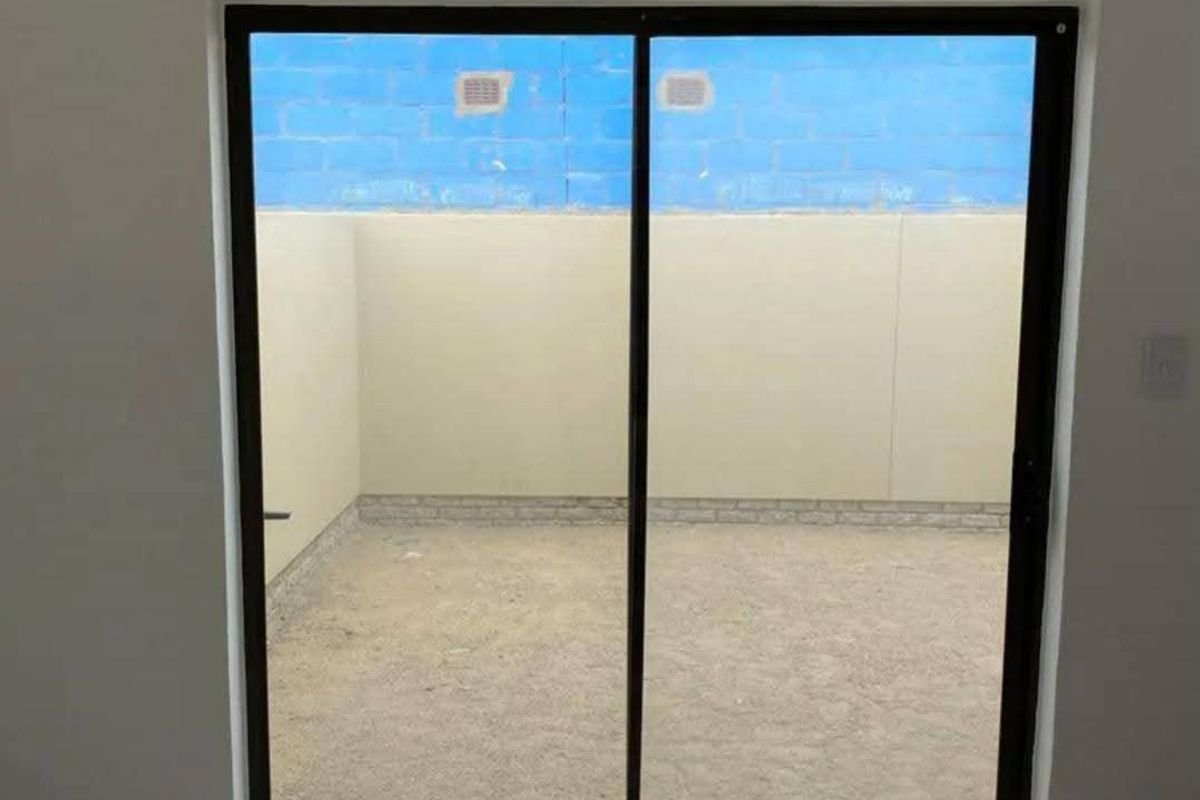 An empty interior space featuring tiled flooring and a sliding glass door leading to a private, walled outdoor courtyard area.