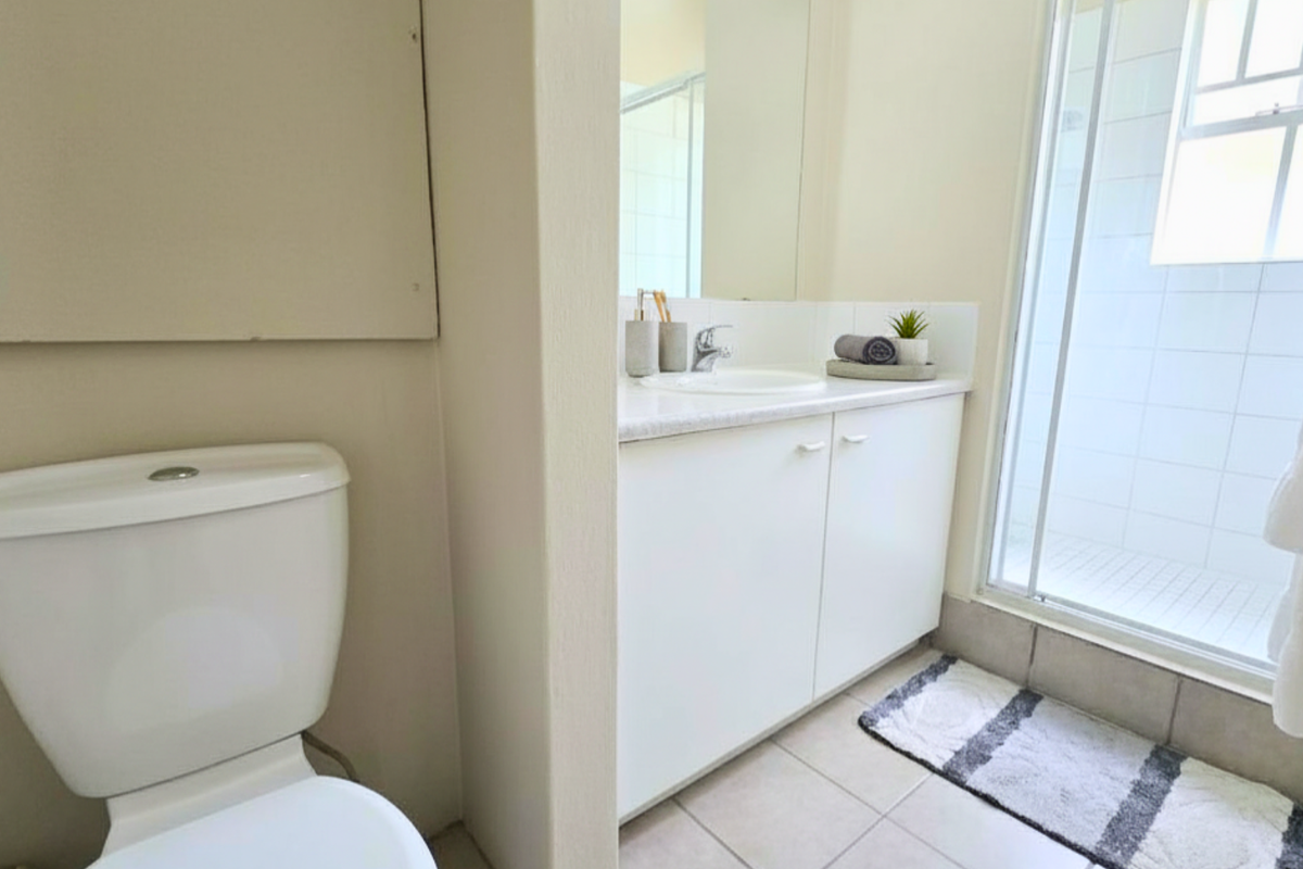 A functional bathroom featuring a white vanity with integrated basin, a glass-enclosed shower, and a standard toilet.
