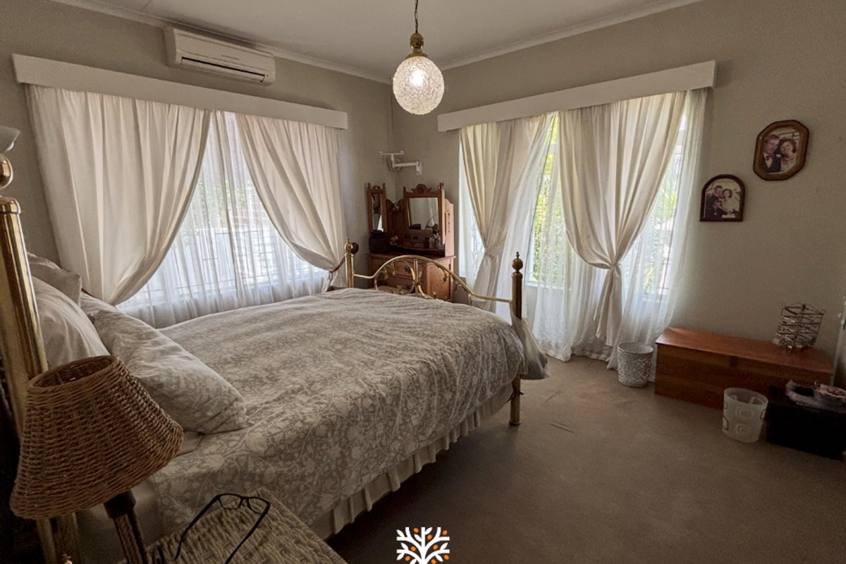 A spacious bedroom featuring carpeted flooring, dual window treatments, and a wall-mounted split-system air conditioning unit.
