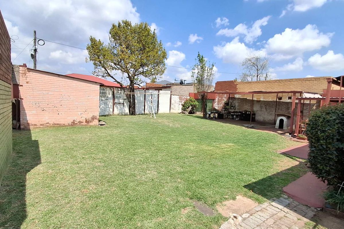 A spacious rear garden featuring a large lawn, brick boundary walls, and a covered patio area, offering potential for outdoor landscaping and entertainment.