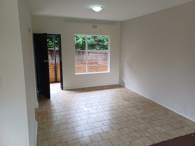 An empty living room featuring tiled flooring, neutral walls, and a window providing natural light, with direct access to an outdoor area.