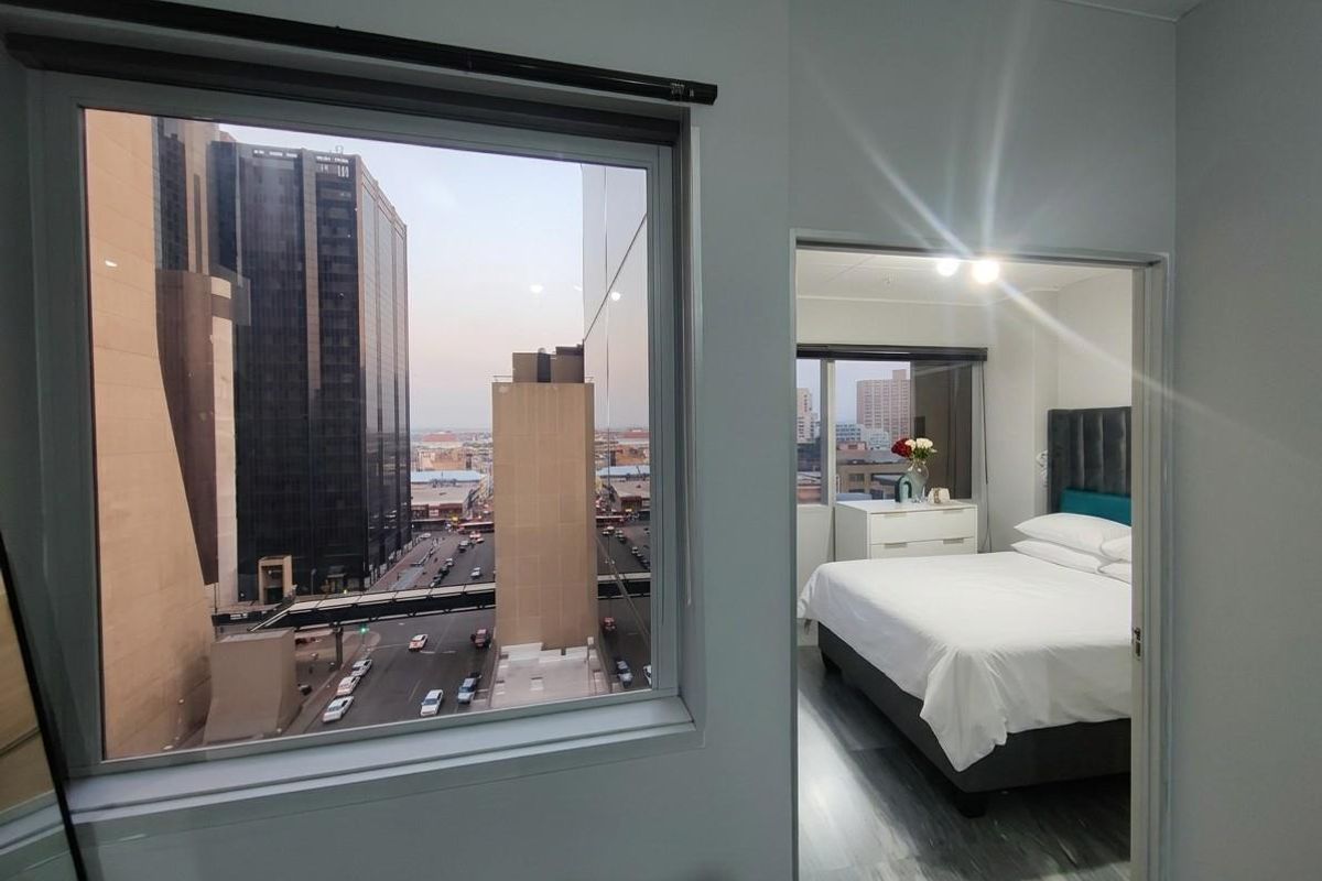 A bedroom featuring large windows with an urban city view, neutral wall finishes, and modern laminate flooring.
