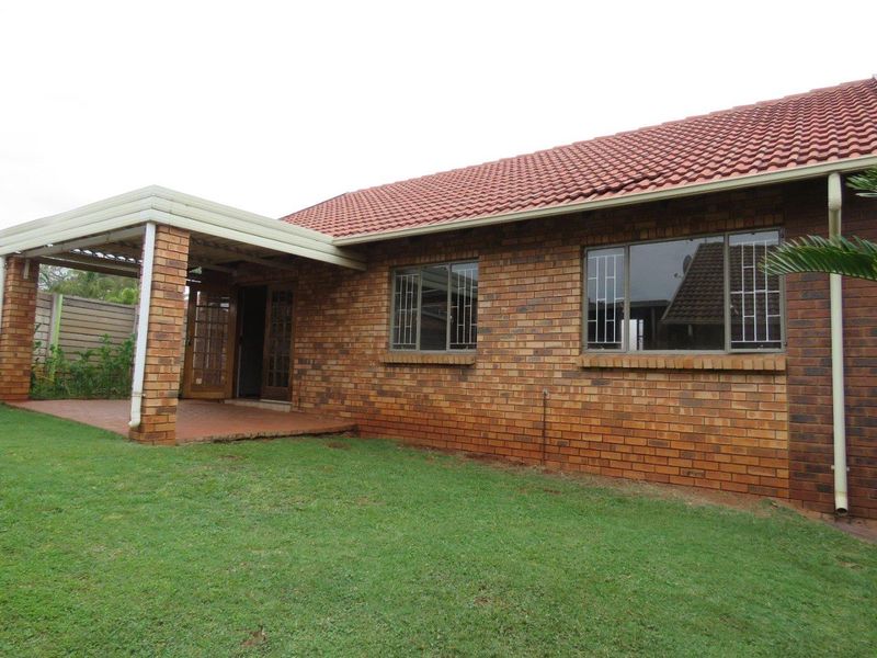 Rear view of the townhouse featuring a face brick facade, tiled roof, and a covered patio area overlooking the garden.