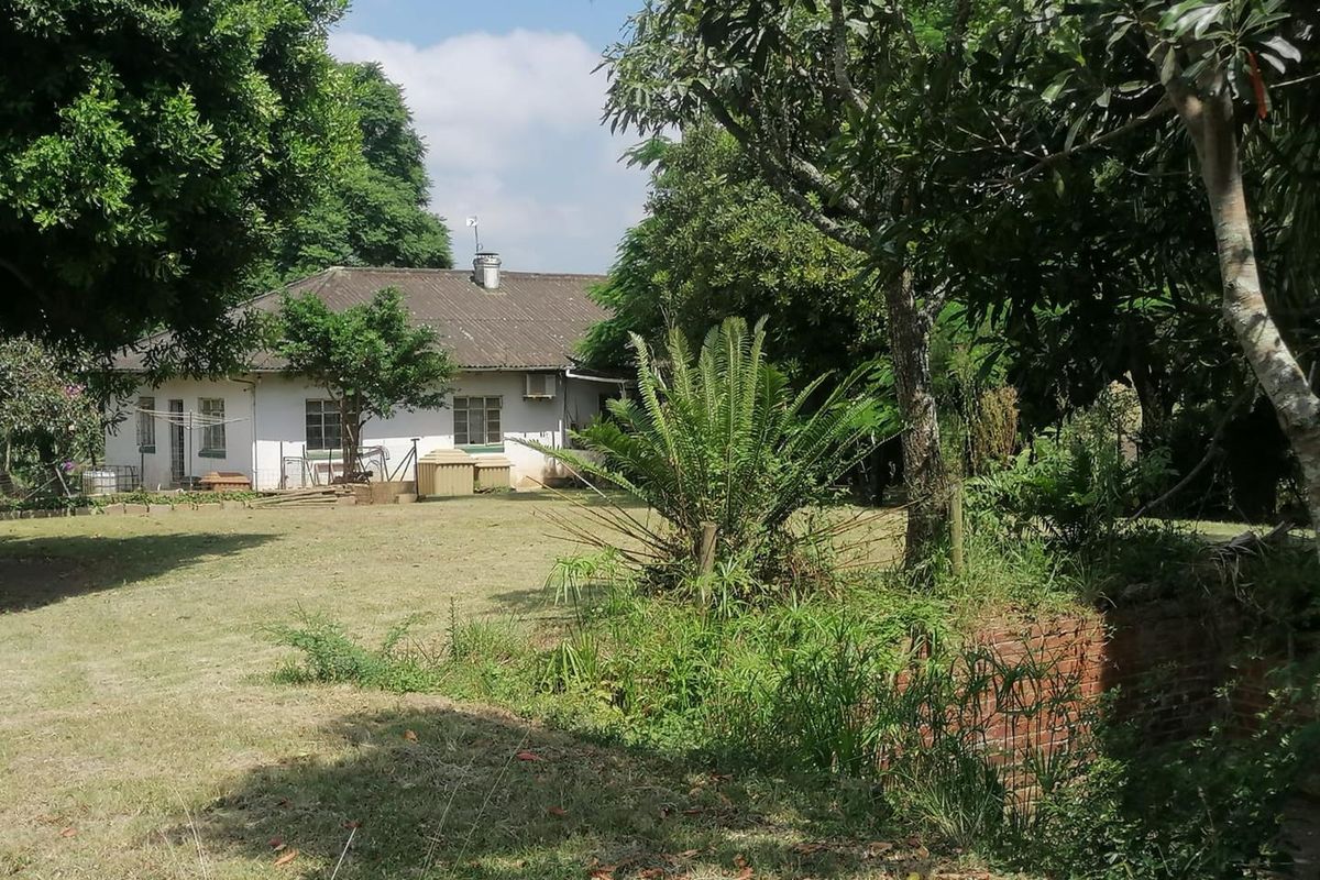 A view of the rear elevation of the property, featuring a tiled roof, brick construction, and a spacious garden area with mature trees.