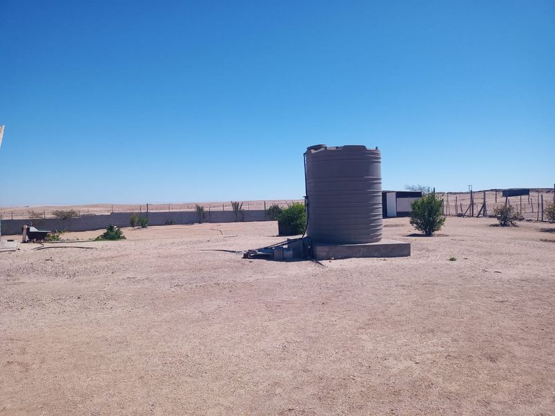 An expansive outdoor area featuring a large water storage tank mounted on a concrete plinth, set within a fenced property boundary.