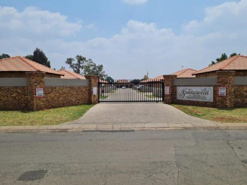 Front entrance view of Sandalwood Estate featuring a secure gated access point, brick boundary walls, and tiled roof architecture.