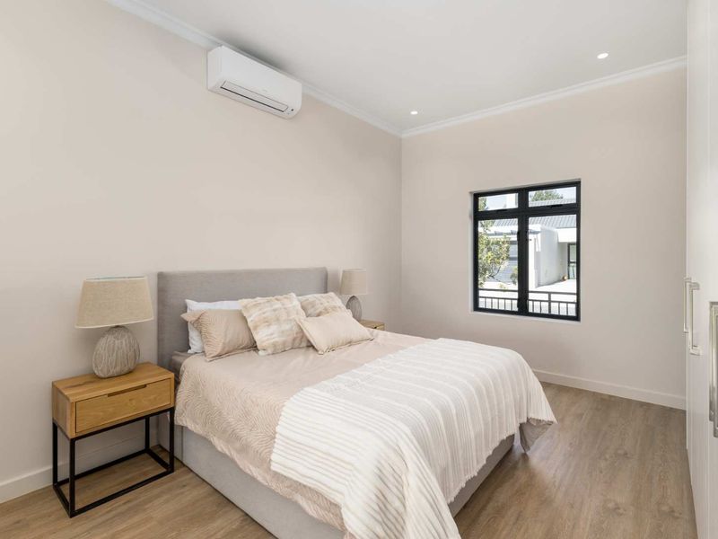 A modern, well-maintained bedroom featuring laminate flooring, built-in wardrobes, recessed lighting, and a wall-mounted air conditioning unit.