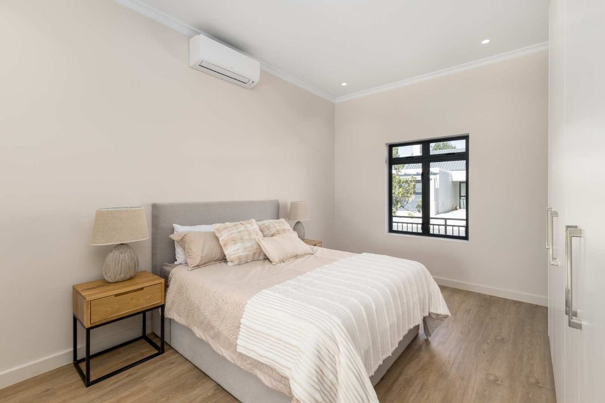 A modern, well-maintained bedroom featuring laminate flooring, built-in wardrobes, recessed lighting, and a wall-mounted air conditioning unit.