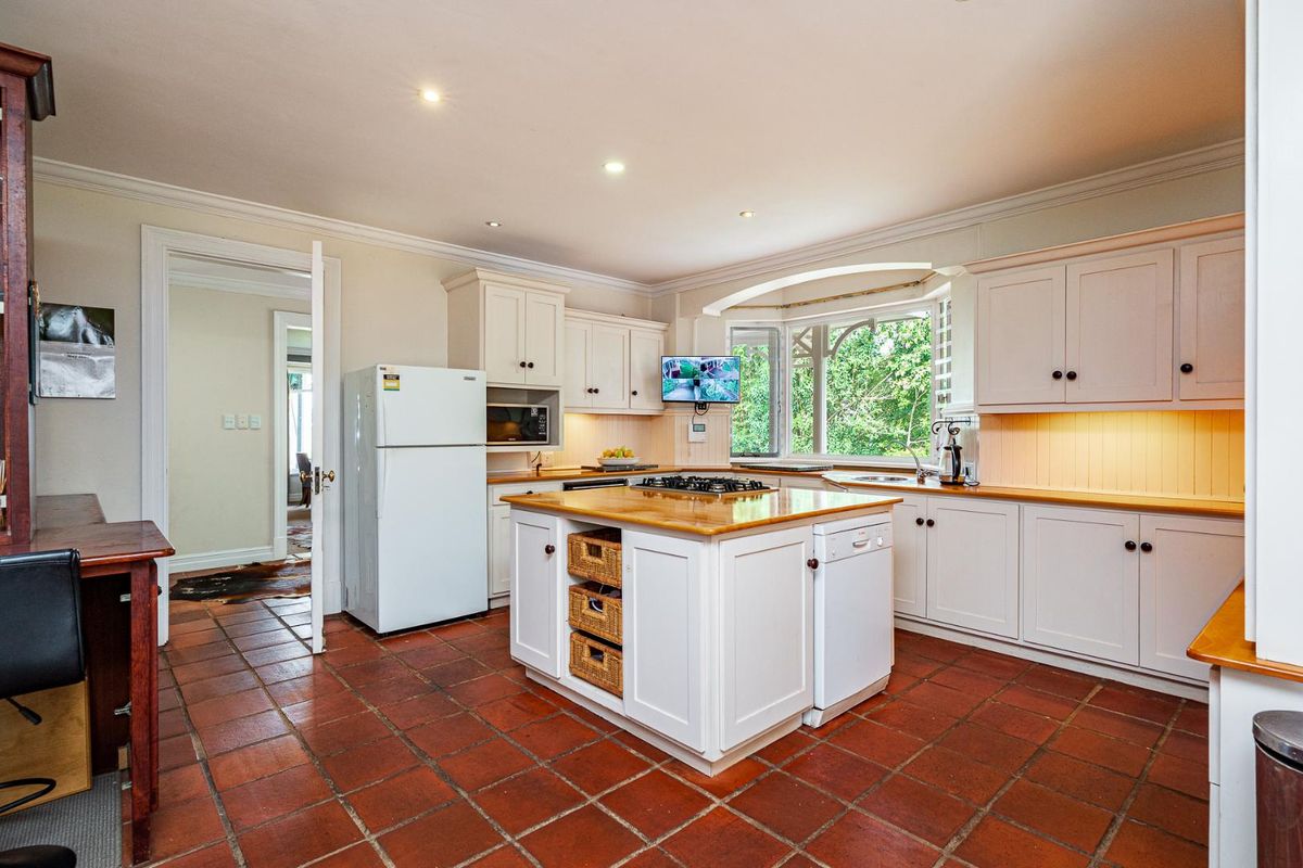 A well-maintained kitchen featuring white cabinetry, timber countertops, a central island with a gas hob, and classic terracotta floor tiles.