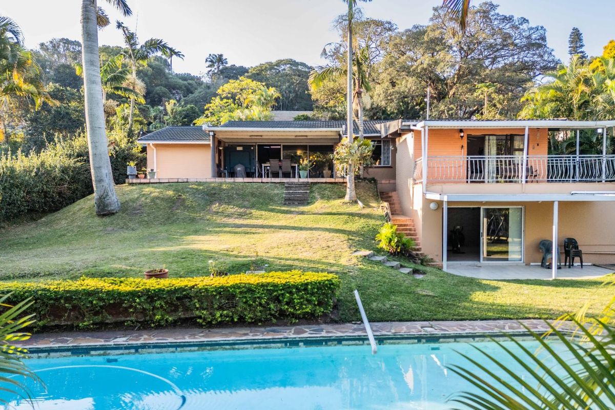 Rear view of a multi-level house featuring a swimming pool, covered patio, balcony, and landscaped garden area.