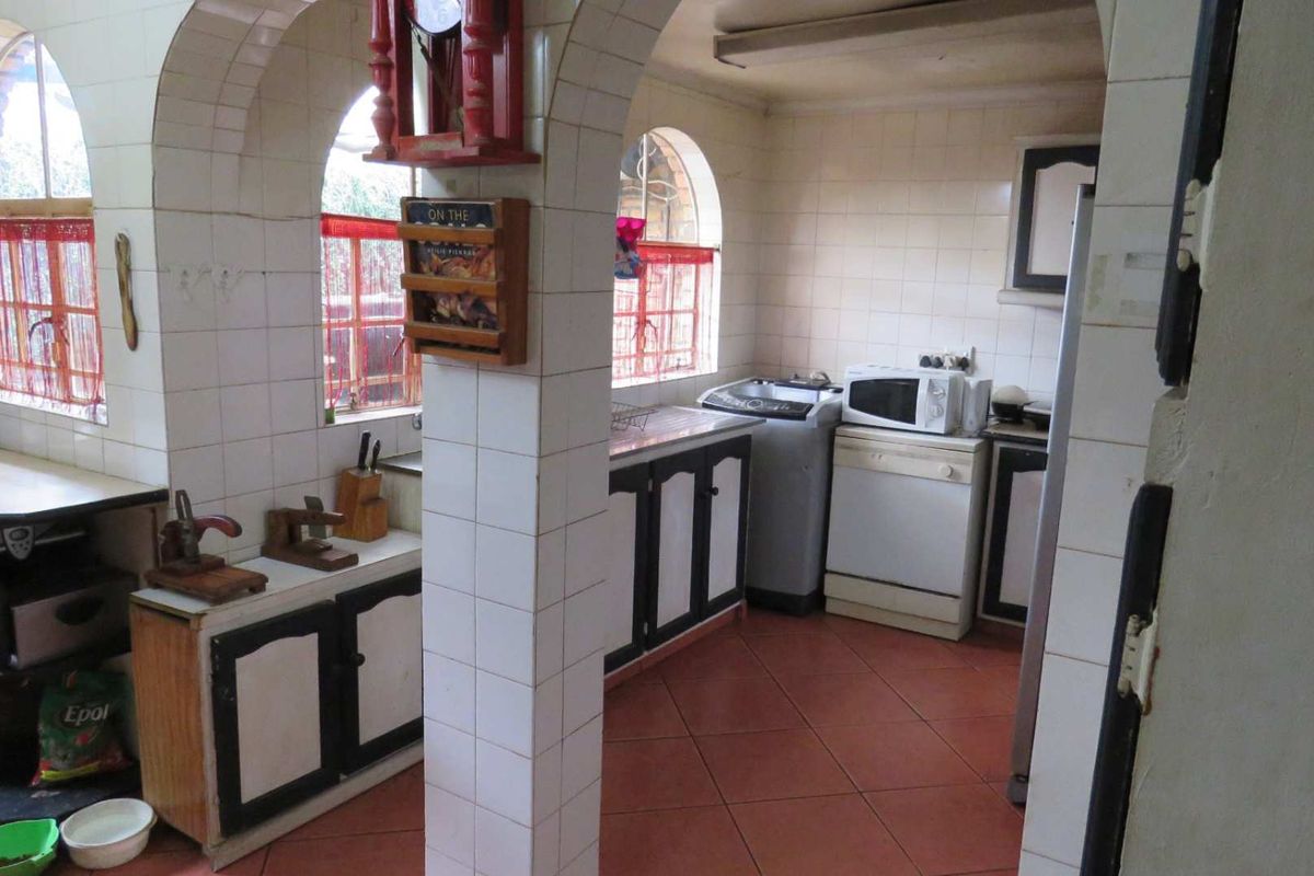 A dated kitchen featuring tiled walls, arched window openings, and built-in cabinetry with a tiled floor, offering potential for a modern renovation.
