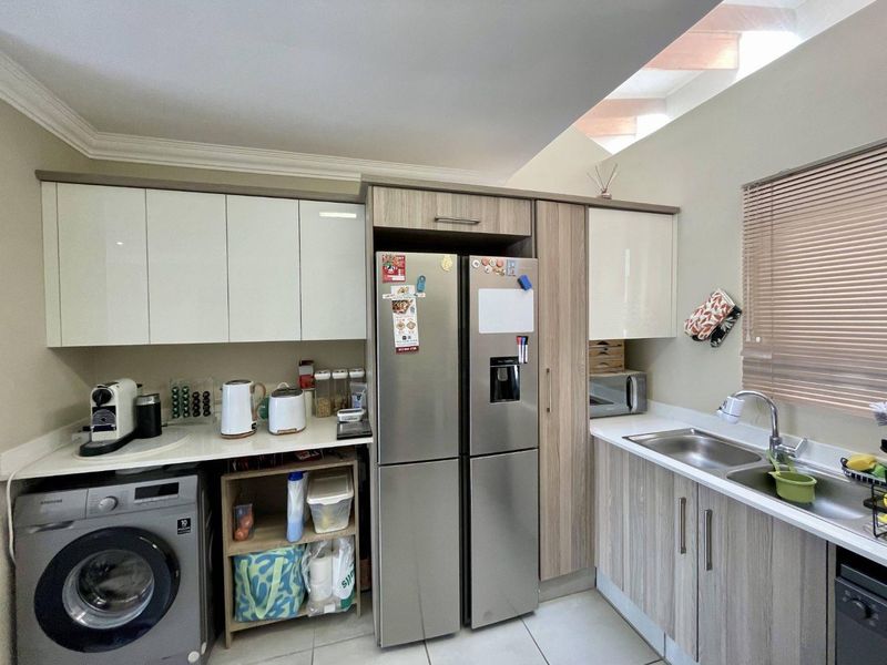 A functional kitchen featuring modern wood-veneer and high-gloss cabinetry, stainless steel sink, tiled flooring, and integrated space for laundry appliances.